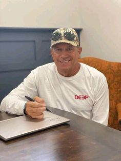 a man sitting at a table with a laptop and pen in his hand while smiling