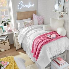 a bedroom with white and pink bedding, pillows and blankets on top of the bed