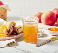 there is a jar of honey next to some peaches and other fruit on the table