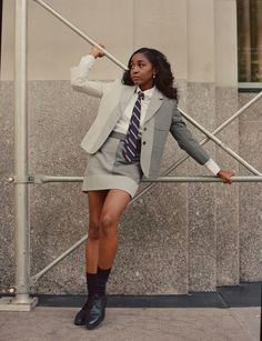 a woman in a short skirt and blazer leaning against a metal fence with her arms behind her back