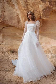 a woman in a white wedding dress standing on the sand near some rocks and cliffs