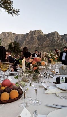 a group of people sitting around a table with food and wine glasses on top of it