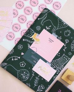 a binder, rubber stamp and some other items on a pink tablecloth with black and white designs