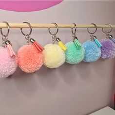 six pom - pom key chains hanging from a wooden bar in front of a wall