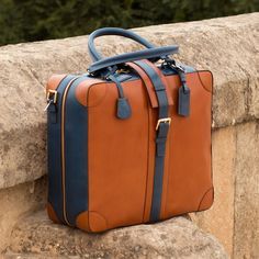 Ideal for the business traveler, the Travel Tote with the classic name tag and leather handles gives you that timeless briefcase style, measuring 14.2 x 16.5 x 6.3 inches / 36 x 42 x 16 cm. It has a main zip closure with a locking buckle strap to secure it. Designed to be functional and minimalist, it features an internal zipped pocket and a full lined interior. The removable shoulder strap makes it perfect for hands-free travel. THE DETAILS: Materials: cognac painted calf + navy painted calf Li Luxury Travel Laptop Bag With Leather Handles, Classic Travel Tote Briefcase, Classic Travel Briefcase Tote, Travel Briefcase With Leather Trim And Top Handle, Business Tote Briefcase With Leather Trim, Luxury Travel Satchel Briefcase, Luxury Travel Briefcase With Leather Trim, Luxury Satchel Briefcase For Travel, Business Briefcase With Leather Trim Tote