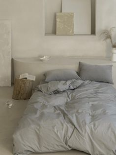 an unmade bed in a white room with two paintings on the wall above it