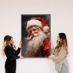 two women standing next to each other in front of a christmas painting on the wall