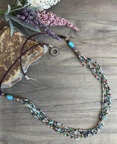 the beaded necklace is sitting on top of a rock next to flowers and leaves