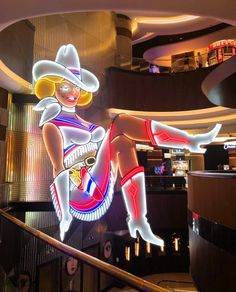 a woman in a cowboy hat is sitting on the stair case next to a neon sign