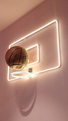 a basketball sitting on top of a neon light in the corner of a room with pink walls