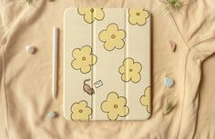 an ipad case sitting on top of a bed covered in flowers and leaves, next to a pencil