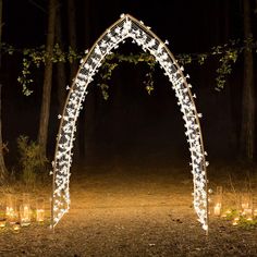 a lighted archway in the middle of a forest at night with candles lit up all around it