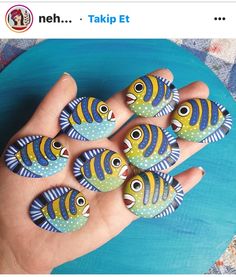 a person's hand holding five painted fish rocks