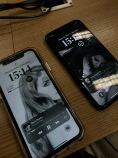 two cell phones sitting next to each other on top of a wooden table in front of a charger