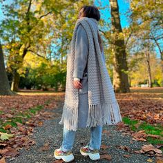 a woman standing in the middle of a leaf filled park wearing a gray coat with fringes