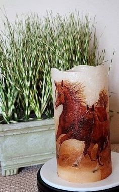 there is a candle with two horses on it next to a potted plant in the corner