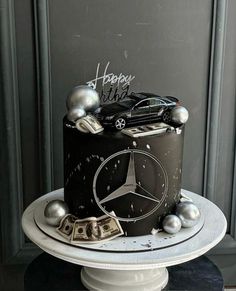 a black and white birthday cake with silver decorations on the top is decorated with a mercedes logo