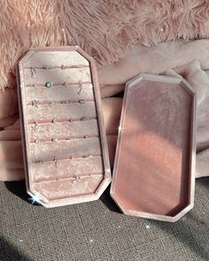 two pink jewelry boxes sitting next to each other on a bed covered in furs