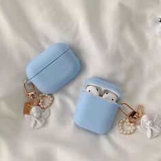 two blue airpods with charms attached to them sitting on a white bed next to each other