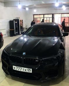 a black car parked in a garage next to two other cars and people looking at it