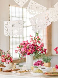 pink flowers are in vases on a table with plates and bowls full of food