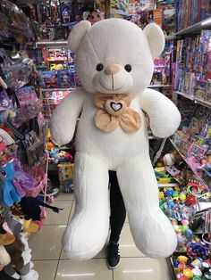 a large white teddy bear with a bow around its neck in a toy store aisle