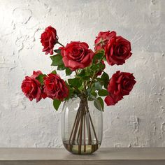 a vase filled with red roses sitting on top of a wooden table next to a white wall