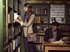 a woman standing in front of a bookshelf with two men sitting at a desk