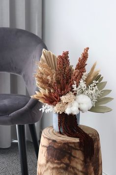 a vase filled with dried flowers sitting on top of a wooden table next to a chair