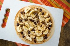 a pizza with bananas and raisins on it sitting on top of a cutting board