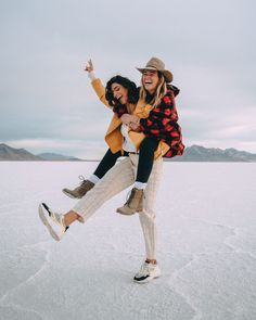 two people are jumping in the air on an ice covered field with mountains in the background