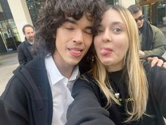 two people taking a selfie in front of a building with other people behind them