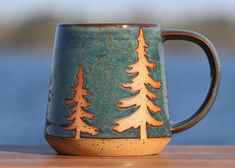 a green and brown coffee mug with trees on the inside sits on a table next to water