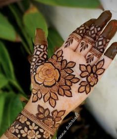 a woman's hand with henna tattoos and flowers on the palm, in front of some plants