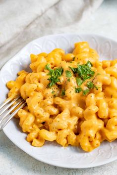 a white plate topped with macaroni and cheese covered in parsley next to a fork