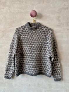 a gray and white sweater hanging on a wall with a pink ball in the corner