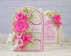 two cards with pink flowers on them sitting on a lace doily covered tablecloth