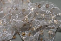 some white and gold fabric with small flowers on the bottom, along with sequins