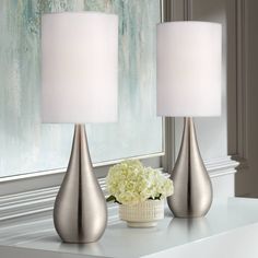 two silver vases with white flowers in them on a table next to a mirror