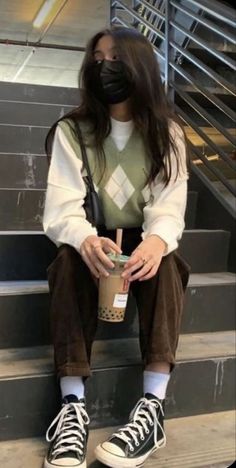 a woman wearing a face mask sitting on the stairs with a cup of coffee in her hand