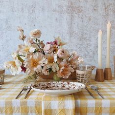 a table topped with flowers and candles next to a vase filled with flowers on top of a checkered table cloth