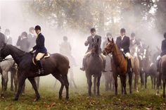 a group of people riding on the backs of horses in a foggy field next to trees