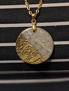 a gold and white necklace on a black and white striped surface with a circular pendant hanging from it