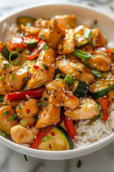 a white bowl filled with chicken and veggies over rice covered in sesame seeds