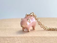 a small pink pig charm sitting on top of a wooden table next to a chain