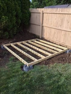 a wooden bed frame sitting in the middle of a yard next to a fence and grass