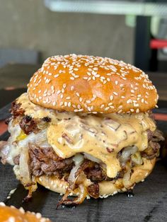 a cheeseburger with meat, onions and sauce on a black plate next to some fries