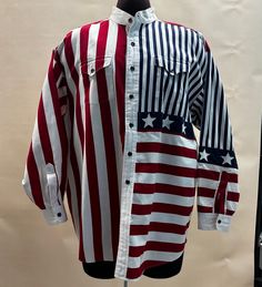 Get ready for Flag Day and the Fourth of July in this fantastic U.S.A. flag long sleeve shirt.  Manufactured by "Panhandle Slim" probably in the 2000's.  Constructed of a heavier cotton, it has long sleeves and a band collar.  It has two flap pockets with button closures. The label has it as as XXL. There is minor staining/discoloration on the neck. Measurements: Armpit to Armpit:  56"  (measured flat then doubled) Waist:  56"  (measured flat then doubled) Hip:  56"  (measured flat then doubled) Flag Day, Nape Of Neck, The Fourth Of July, Cotton Long Sleeve Shirt, Band Collar, Mens Oxfords, Usa Flag, Flap Pocket, Sleeve Cotton