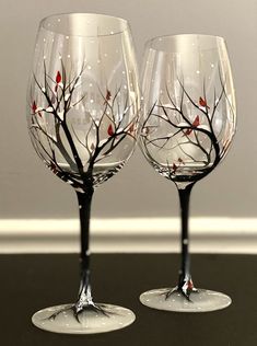 two wine glasses with branches painted on them sitting on a table next to each other