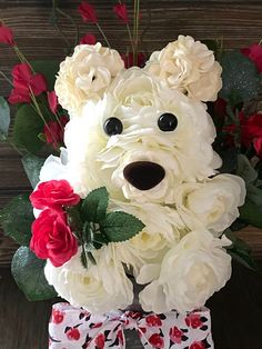 a teddy bear made out of white flowers and greenery with red roses in the background